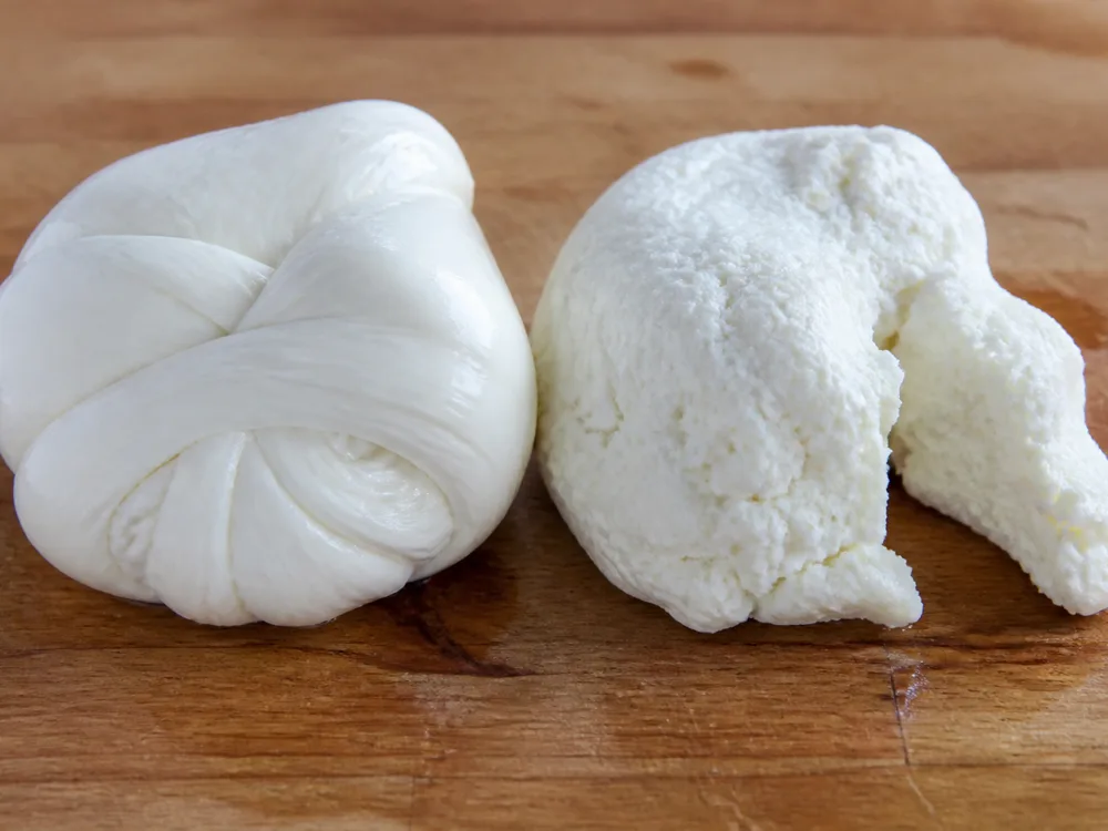 A smooth stretched piece of mozzarella beside a grainy broken piece - fresh mozzarella | KnowTheCheese