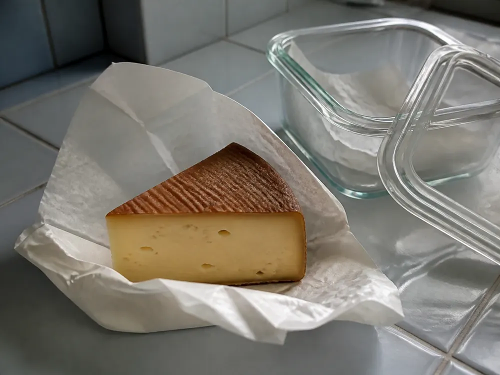 Belval-style wedge on breathable paper beside an open cheese container - Abbaye de Belval | KnowTheCheese