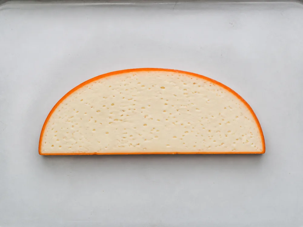 Half disc seen from above with a thin orange rind ring around pale cream paste - Abbaye du Mont des Cats | KnowTheCheese