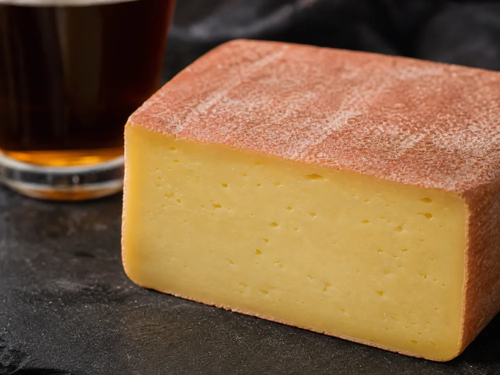 Pink washed rind on an Admiral Collingwood-style square wedge with brown ale nearby - Admiral Collingwood | KnowTheCheese