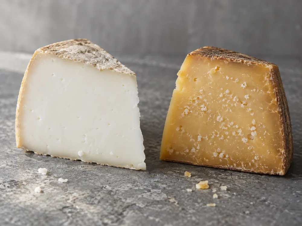 Two cheese wedges side by side, one with snow-white paste and one with golden paste and white crystals - Aged Goat's Cheese | KnowTheCheese