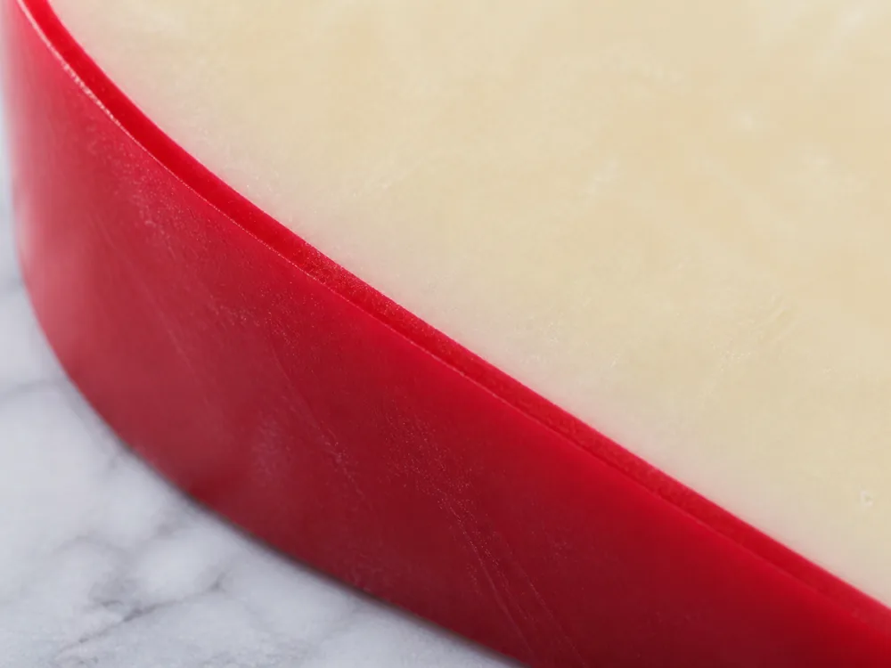 Close cross-section showing the red wax shell sitting directly on pale paste - Airedale | KnowTheCheese