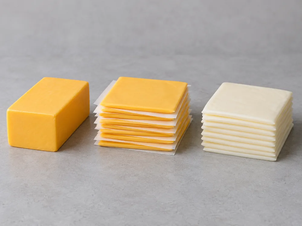 Unsliced block, wax-paper-stacked yellow slices and stacked white slices of American cheese - American Cheese | KnowTheCheese