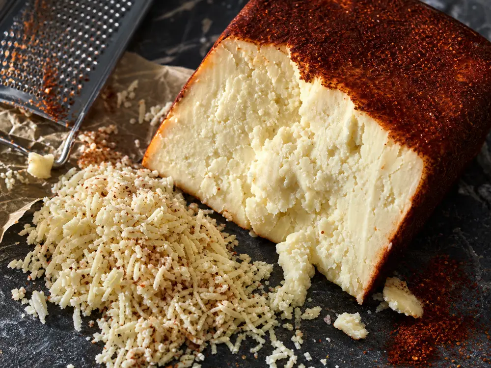 Red-coated firm cheese wedge with grated crumbles - Añejo Enchilado | KnowTheCheese