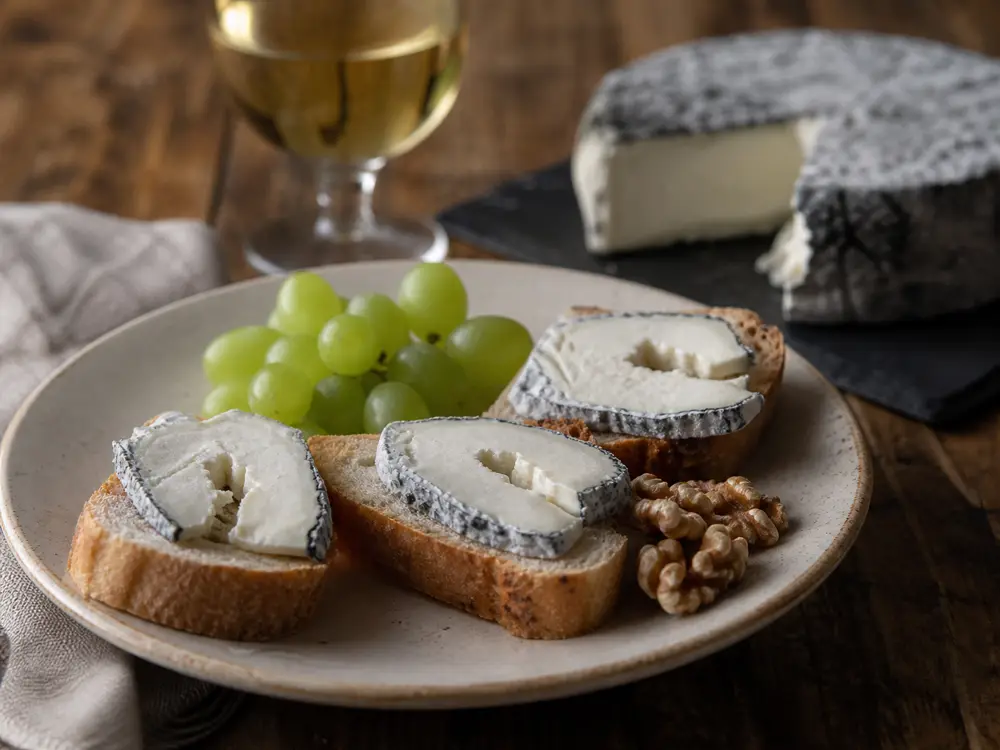 Ash-rind goat cheese ring slices with bread grapes and white wine - Anneau du Vic-Bilh | KnowTheCheese
