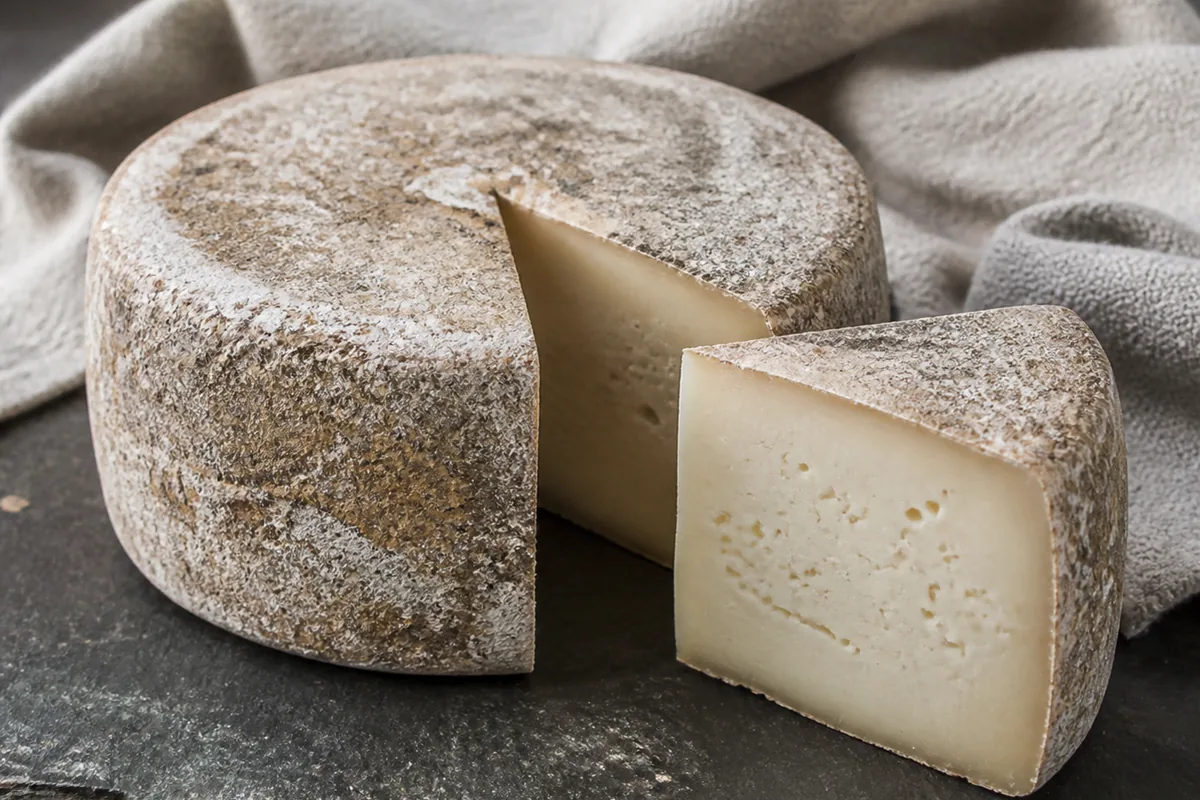 Sheep-milk wheel with mottled natural rind and a cut wedge showing ivory paste - Ardi Gasna | KnowTheCheese