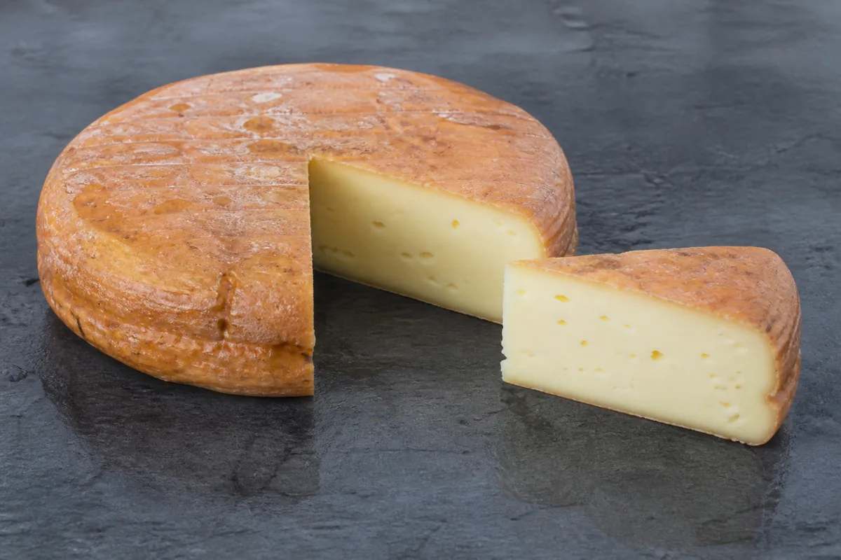 Low wide wheel with a damp orange-brown rind and a wedge showing pale paste with small holes - Ardrahan | KnowTheCheese