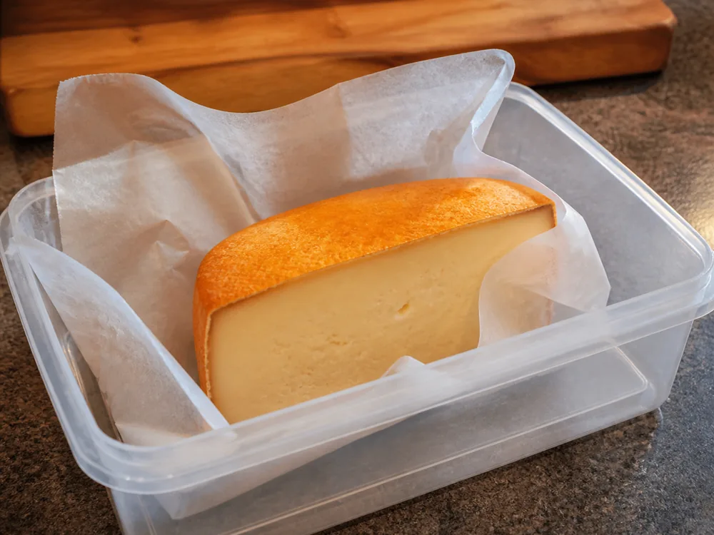 Cut piece on waxed paper inside an open plastic box on a kitchen counter - Ardrahan | KnowTheCheese