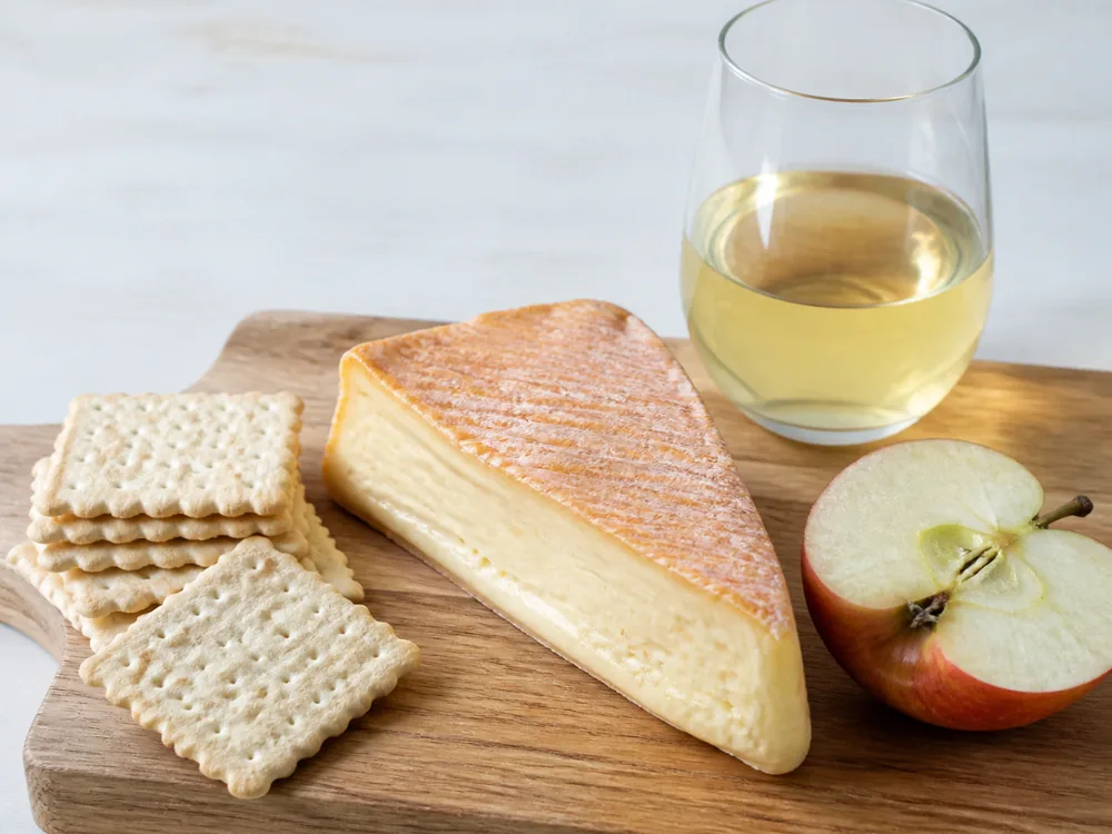 Wedge of orange-rinded cheese on a board with a halved apple, dry cider and plain water biscuits - Ardrahan | KnowTheCheese