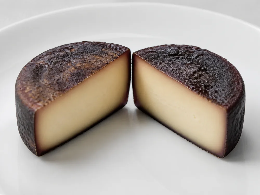 One disc cut in half showing a pale ivory dense paste against a dark stained crust - Aromes au Gene de Marc | KnowTheCheese
