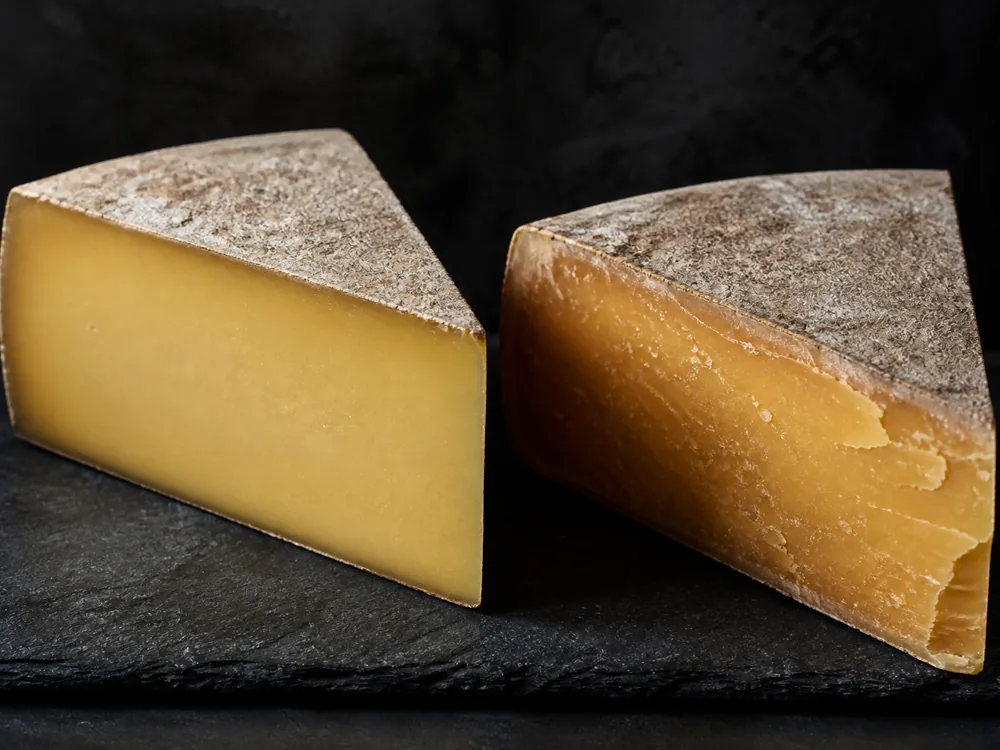 Two wedges on slate, the younger smooth at the cut face and the older Reserve drier and flaking with white crystal specks - Ascutney Mountain | KnowTheCheese