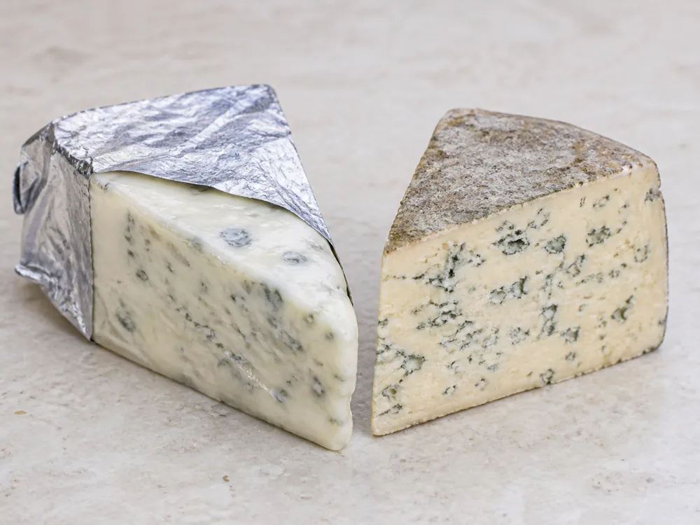 Foil-wrapped blue wedge beside a natural-rind blue wedge with a warmer paste - Asher Blue | KnowTheCheese