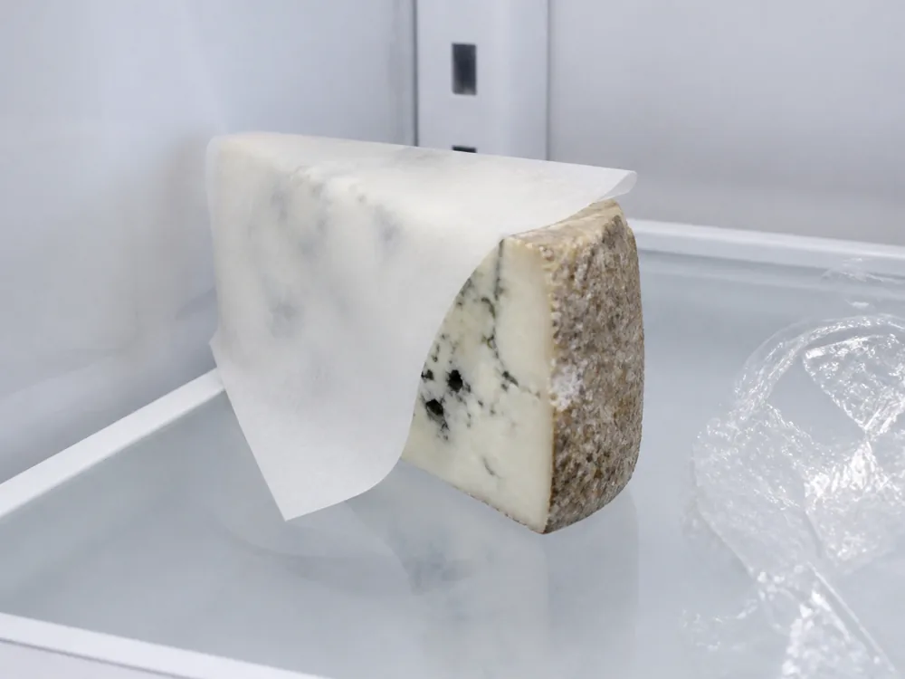 Blue cheese wedge loosely wrapped in waxed paper beside a discarded sheet of cling film - Asher Blue | KnowTheCheese