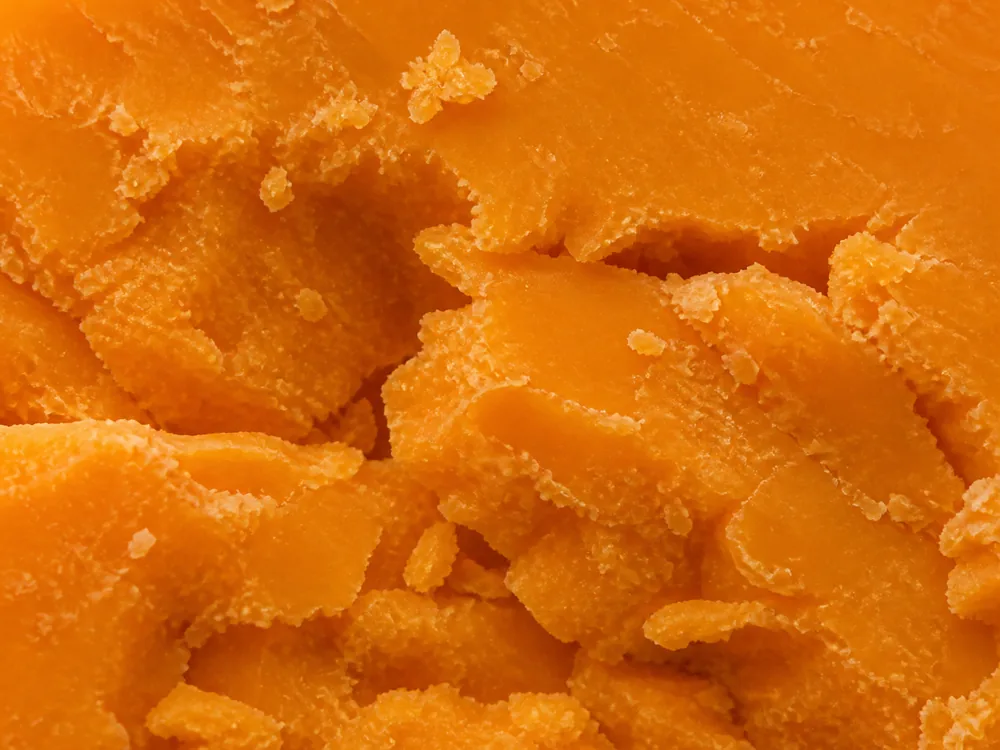 Macro of a deep orange crumbly broken face with loose flakes at the edges - Auld Lochnagar | KnowTheCheese