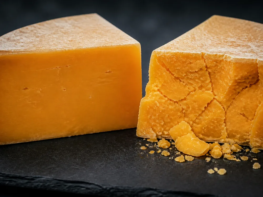 Two deep orange pieces side by side, the younger smooth at the cut face and the aged one broken into crumbs - Auld Lochnagar | KnowTheCheese