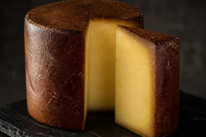 Tall truckle with a deep amber smoked surface and a cut wedge showing pale gold interior - Auld Reekie | KnowTheCheese