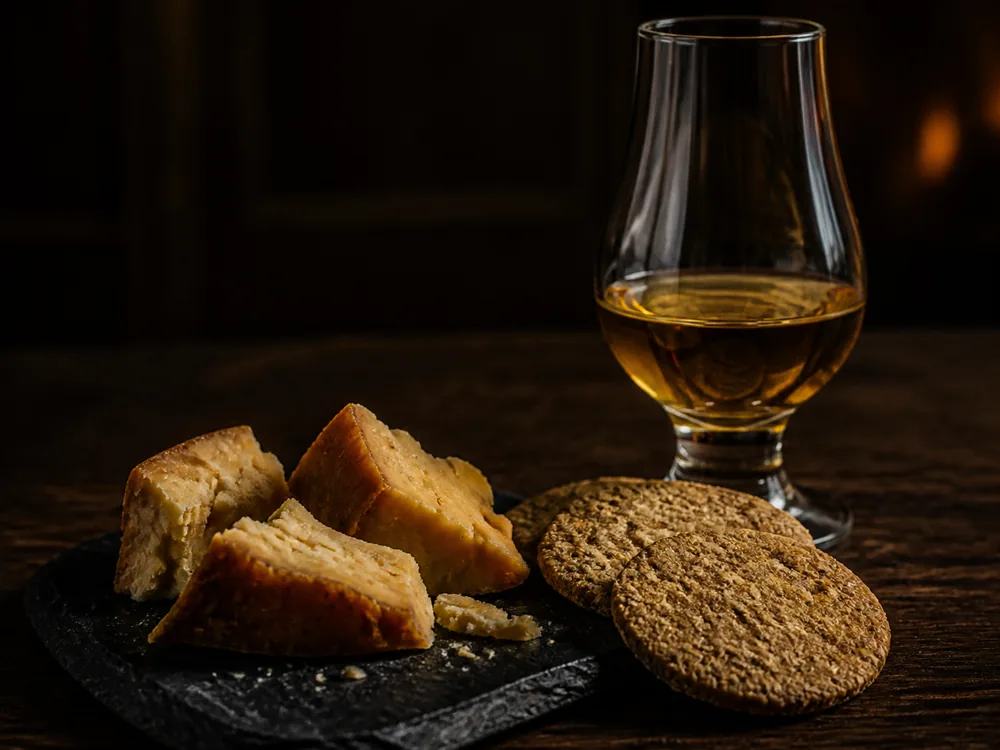 Chunks of smoked cheese on a slate plate beside a dram of whisky in a nosing glass and plain oatcakes - Auld Reekie | KnowTheCheese