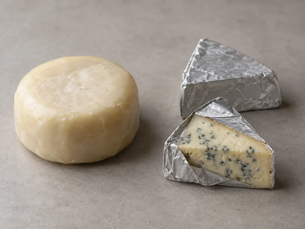 Wax-coated round cheese beside foil-wrapped blue cheese wedges - Aura Cheese | KnowTheCheese
