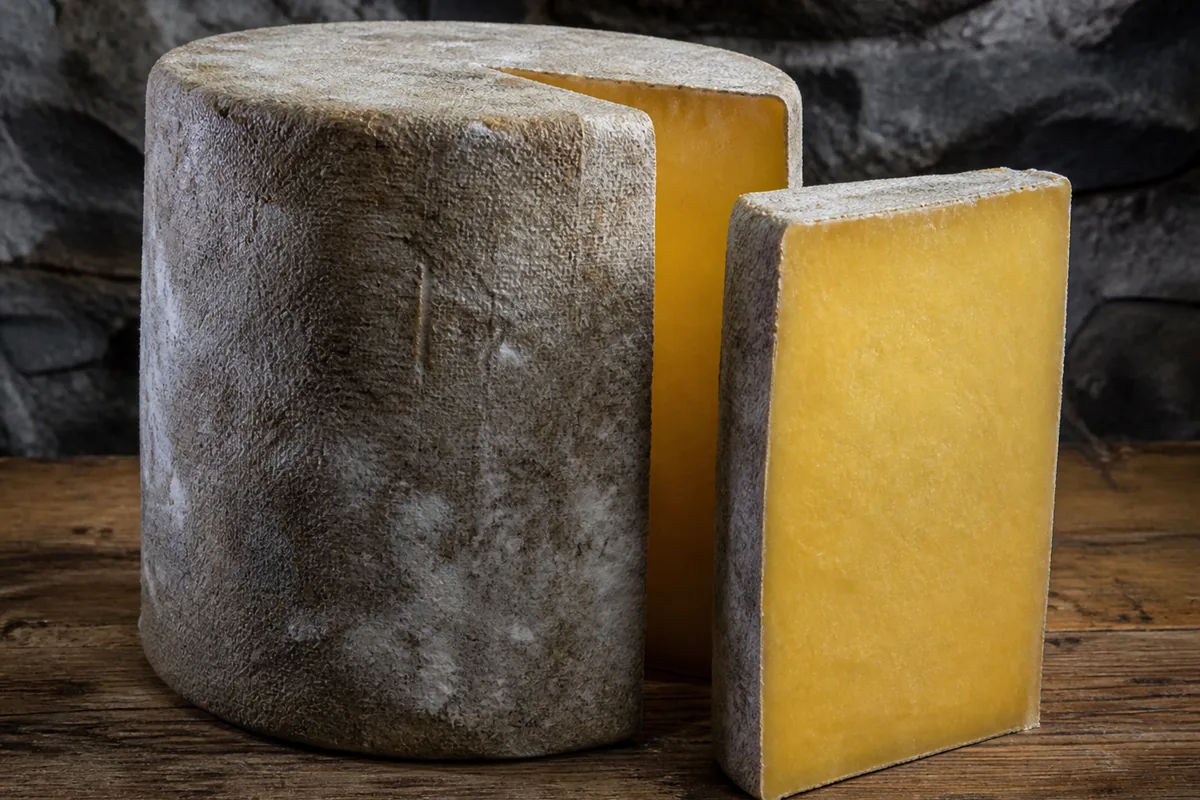 Cloth-bound cheddar wheel with a cut wedge showing deep golden paste - Avonlea Clothbound Cheddar | KnowTheCheese