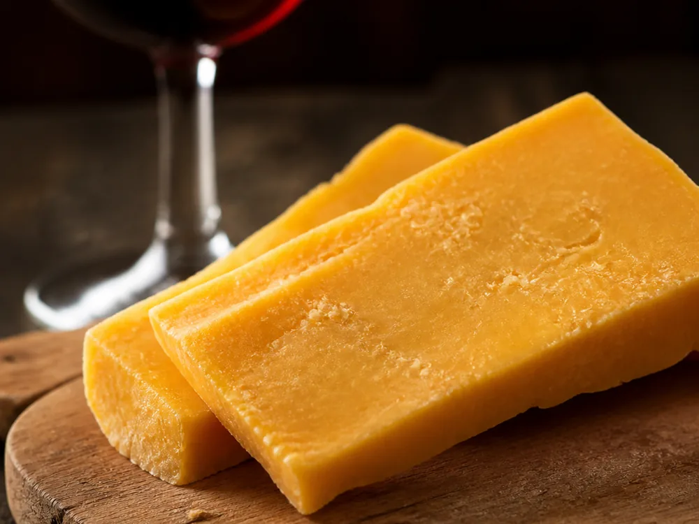 Slices of golden cheddar softened at room temperature beside a glass of light red wine - Avonlea Clothbound Cheddar | KnowTheCheese