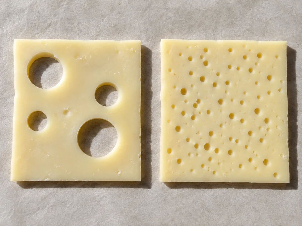 Two cheese slices, one with a few large holes and one with many small close-set holes - Baby Swiss | KnowTheCheese