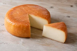 Low round wheel with an orange washed rind and a cut wedge showing smooth ivory paste - Baluchon | KnowTheCheese