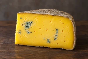 Wedge of buttery golden-yellow cheese with a natural rind and blue mould in a few small patches - Barden Blue | KnowTheCheese