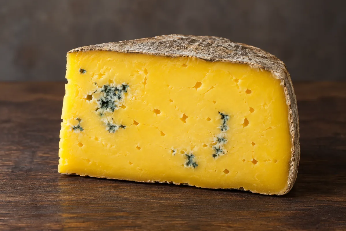 Wedge of buttery golden-yellow cheese with a natural rind and blue mould in a few small patches - Barden Blue | KnowTheCheese