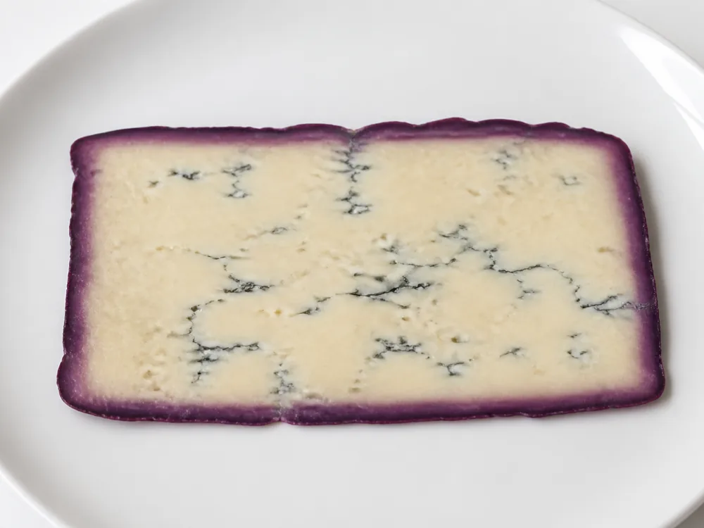 Thin slice showing a purple-stained outer band against a pale veined interior - Basajo | KnowTheCheese