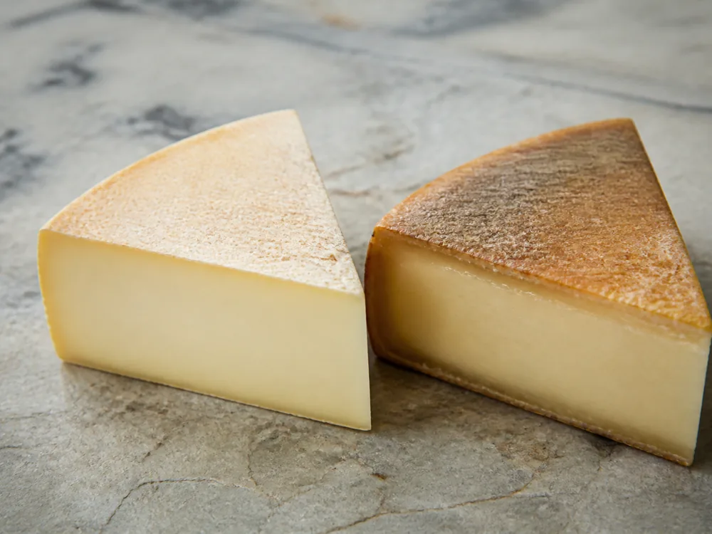 Fresh pale wedge beside one with a dried cracked cut face and darkened rind - Beaumont | KnowTheCheese