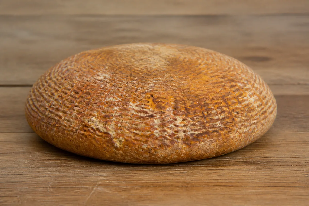 Squat wheel with rusty rind carrying the concentric imprint of a colander - Berkswell | KnowTheCheese