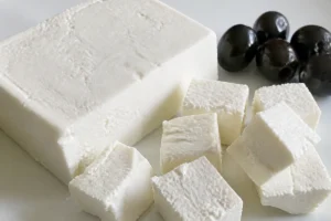 Block of pure white rindless cheese on a plain plate with rough-cut cubes and a few black olives - Beyaz Peynir | KnowTheCheese
