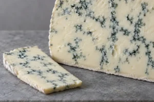 Soft ivory blue-veined cheese with a cut slice beside it - Blue Castello | KnowTheCheese