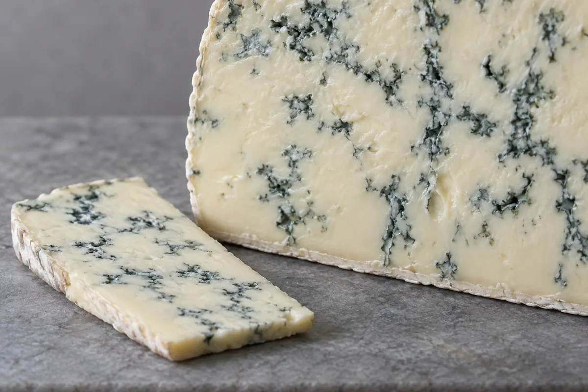 Soft ivory blue-veined cheese with a cut slice beside it - Blue Castello | KnowTheCheese