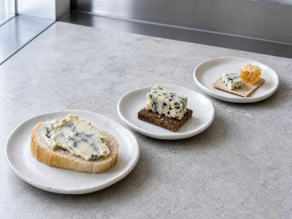 Decreasing portions of creamy blue, Stilton-style cheese, and Roquefort-style cheese on baguette, rye, and cracker - Blue cheese pairing | KnowTheCheese