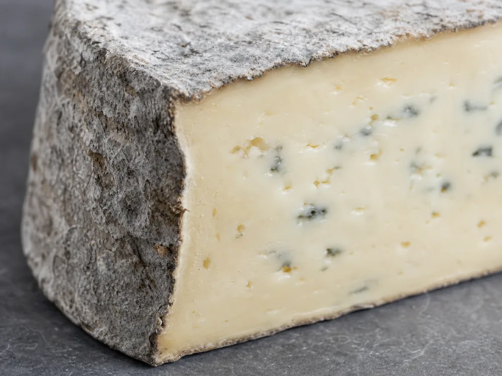 Gray natural rind around the beige paste and pale blue veins of Bluebell cheese