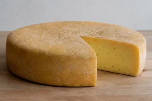 Wide flat Dutch cheese wheel with a dry natural rind and a wedge cut away showing pale gold paste with small round eyes - Boerenkaas | KnowTheCheese