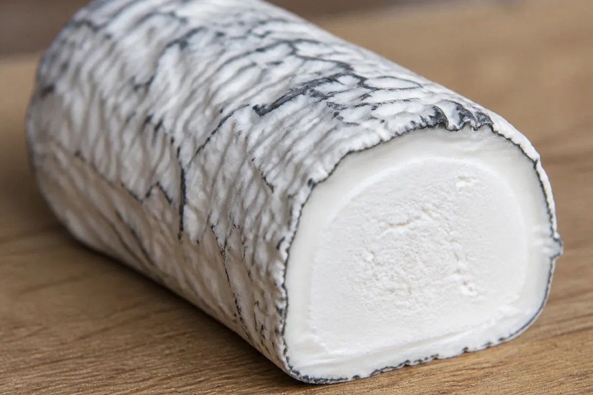 Goat's milk log with wrinkled white rind and dark ash showing through, one end cut to reveal chalk-white paste with a creamier band under the rind - Bosworth | KnowTheCheese