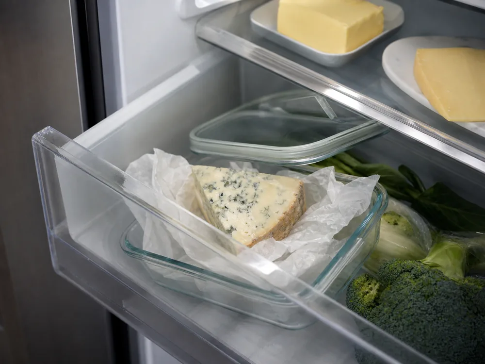 Parchment-wrapped blue cheese wedge in a shallow refrigerator container - Buttermilk Blue Affinee | KnowTheCheese