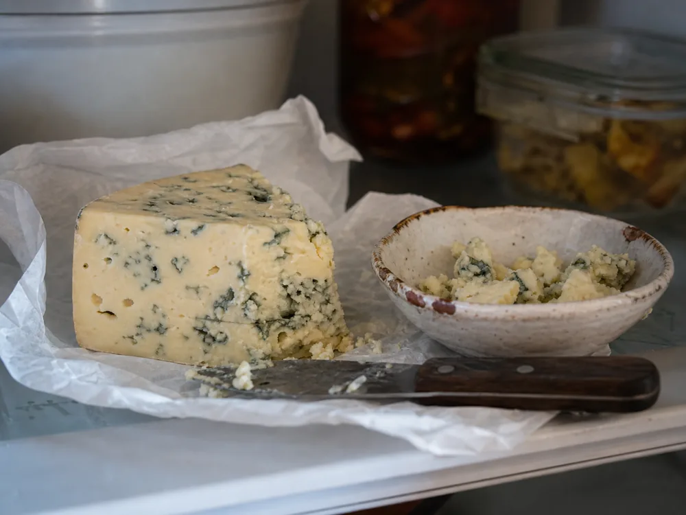 Wrapped Buttermilk Blue wedge beside a bowl of loose crumbles