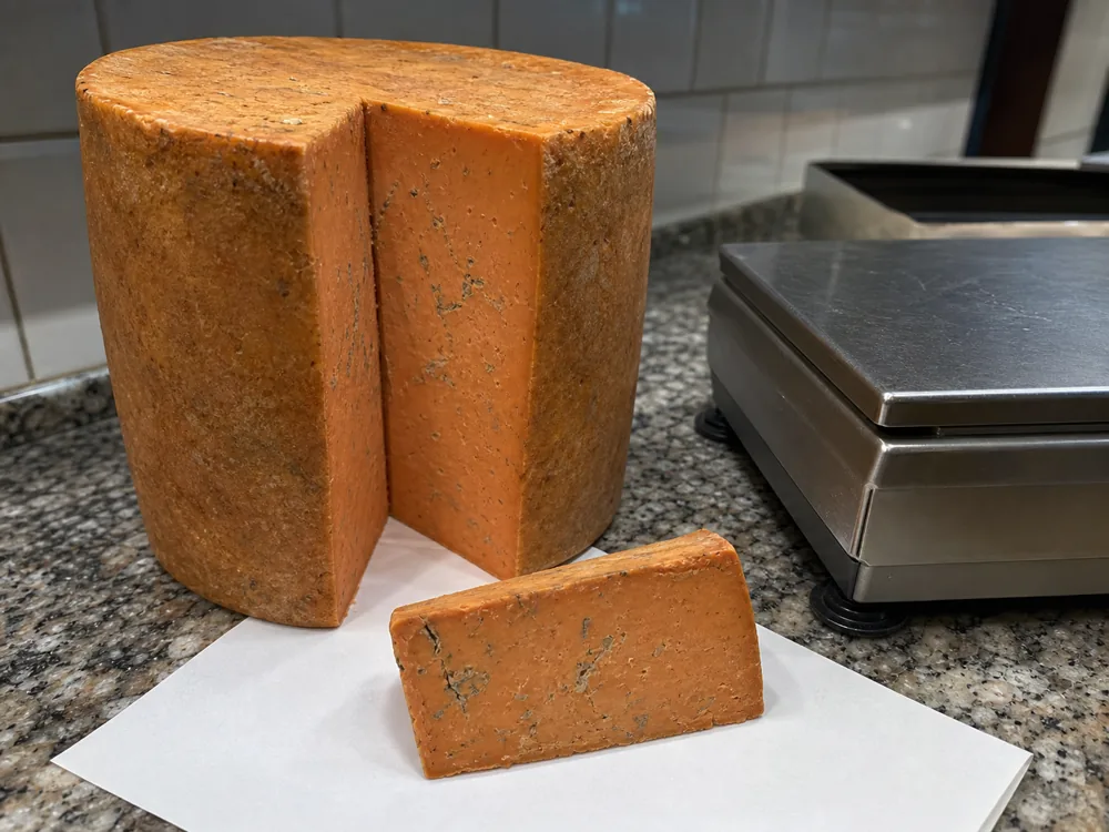 Large russet blue cheese cylinder beside a cut wedge - Buxton Blue | KnowTheCheese
