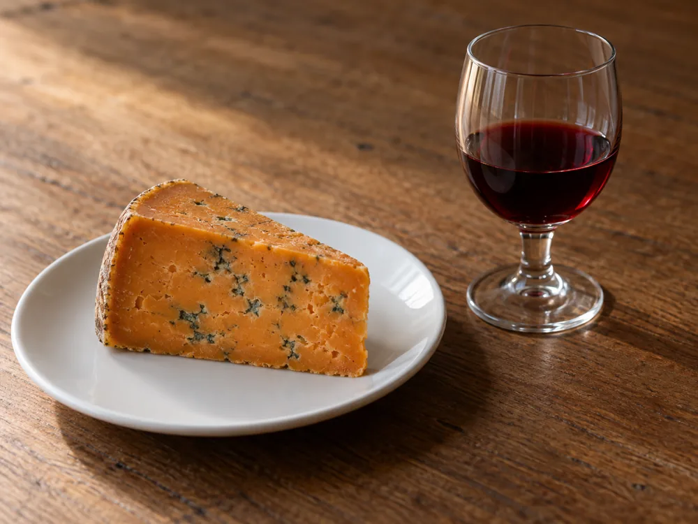 Russet blue cheese wedge on a plate beside a glass of ruby-red port - Buxton Blue | KnowTheCheese