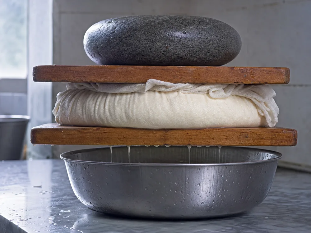 Fresh curd wrapped in cloth and pressed between boards - Byaslag | KnowTheCheese