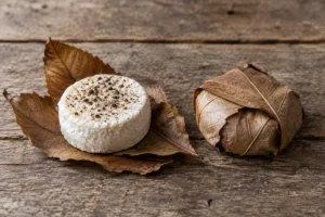 Small peppered white goat cheese on chestnut leaves beside a leaf-wrapped cheese - Cabécou Feuille d'Armagnac | KnowTheCheese
