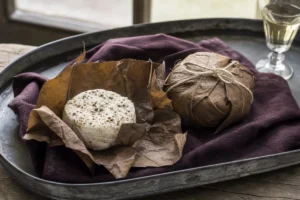 Leaf-wrapped small goat cheese opened beside a peppered white disc - Cabécou Feuille d'Armagnac