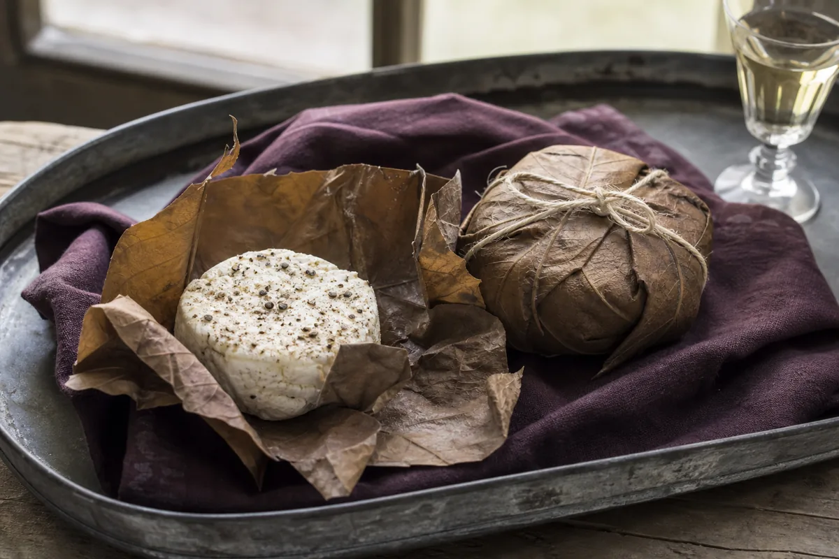 Leaf-wrapped small goat cheese opened beside a peppered white disc - Cabécou Feuille d'Armagnac
