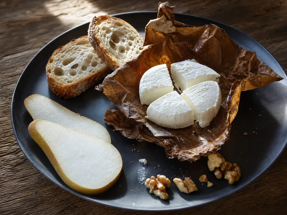 Leaf-wrapped goat cheese portioned with bread pear and walnuts | KnowTheCheese
