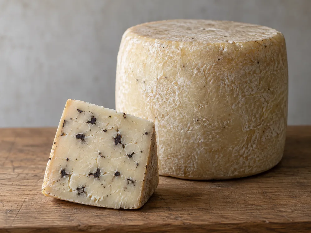 Whole wheel of pale cheese beside a cut wedge with dark truffle flecks - Cacio di Bosco al Tartufo | KnowTheCheese