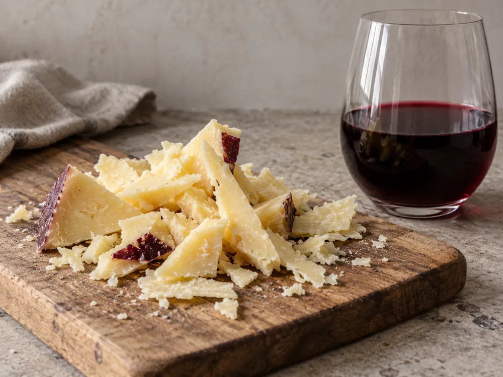 Shreds of light-yellow cheese beside a glass of red wine