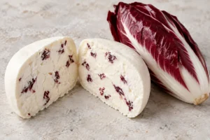 Cut soft white cheese with dried red radicchio pieces beside a Treviso radicchio head - Cacioradicchio | KnowTheCheese